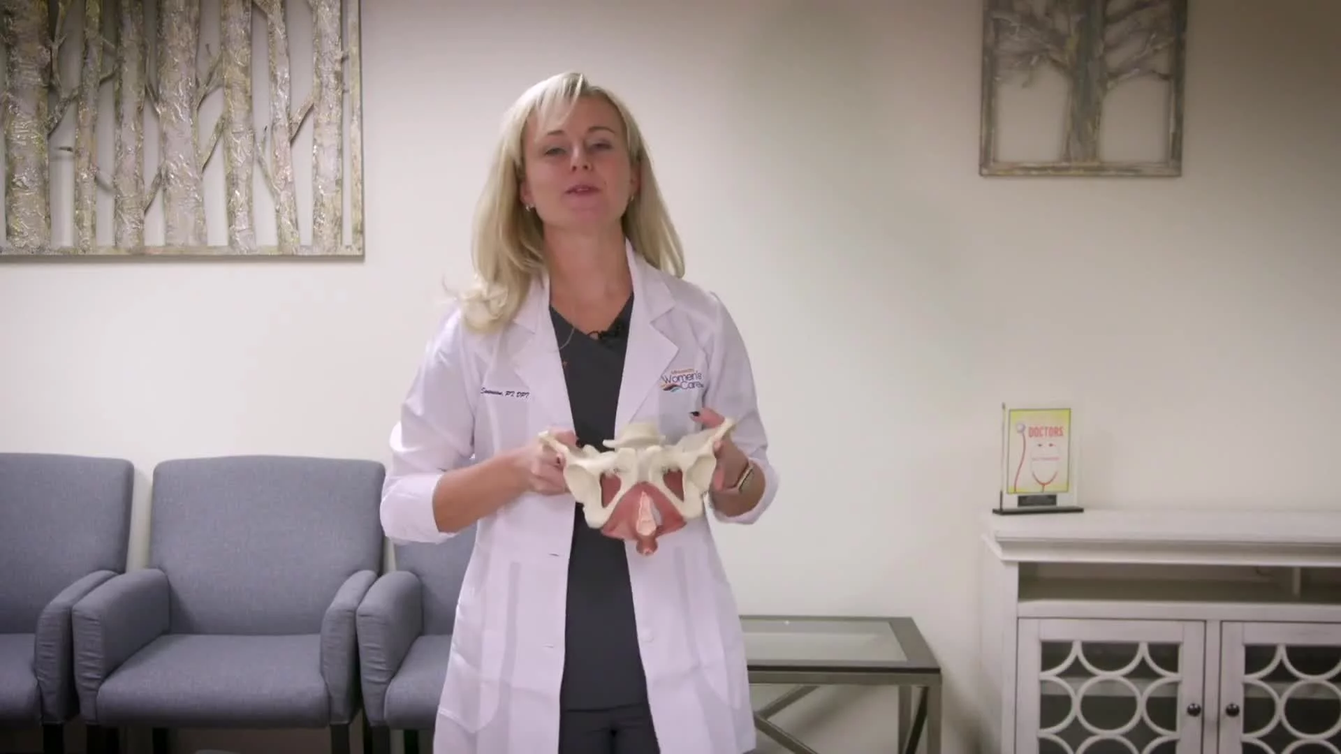 Female doctor holding pelvic model while explaining anatomy in a clinic.