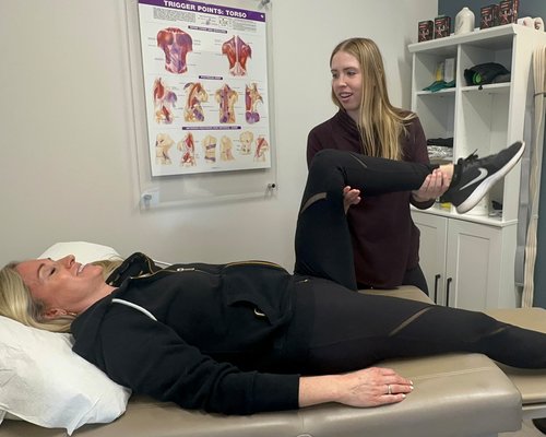 Therapist assisting woman with leg stretch on examination table.