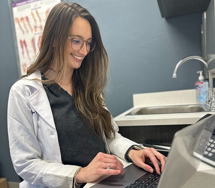 Female doctor smiling while working on a laptop in a clinic.