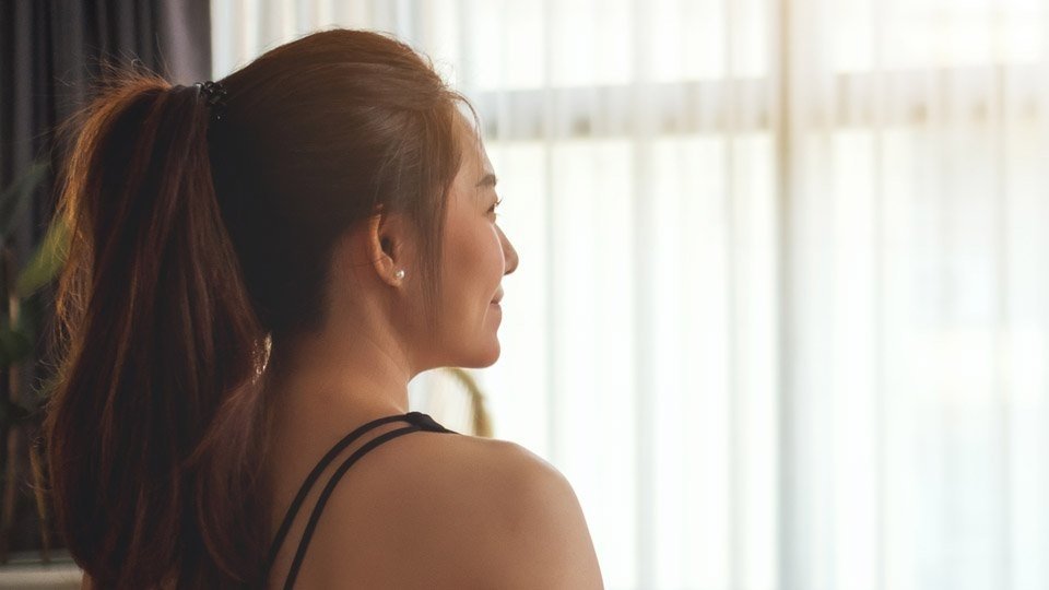 Woman with ponytail smiling while looking out a bright window.