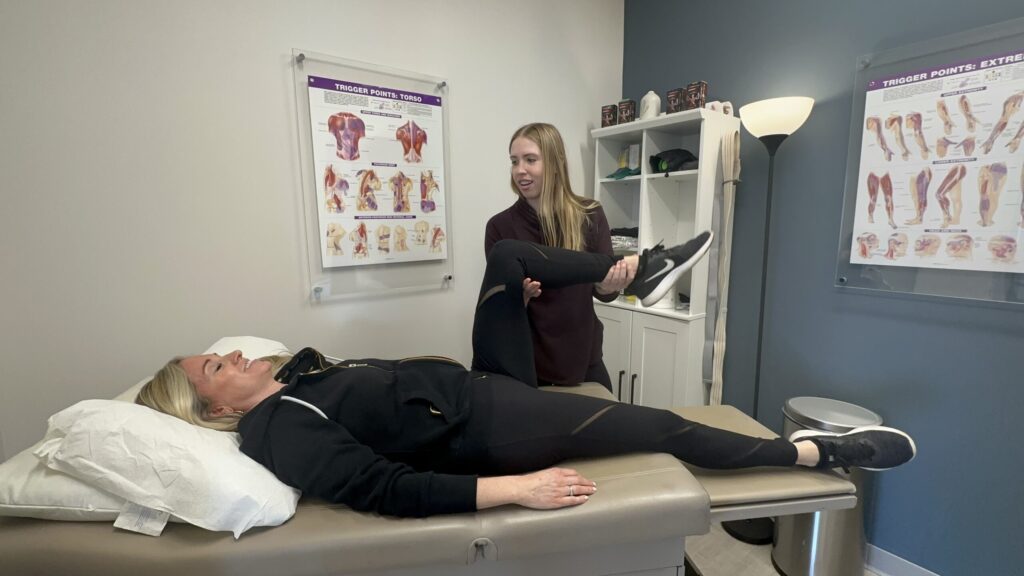 Therapist performing leg stretch on patient lying on examination table.