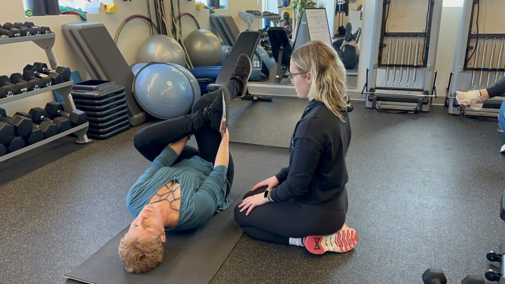 Trainer assisting client with a stretching exercise on a gym mat.
