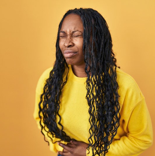 Woman in yellow sweater clutching stomach in visible discomfort or pain.